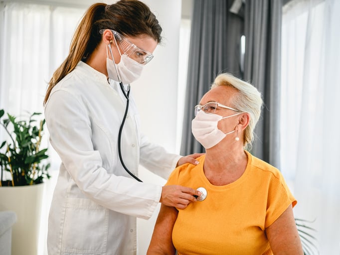 Doctor in protective mask using stethoscope to assess woman patient's heart health