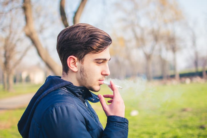Teenage boy smoking a cigarette at risk for poor adolescent dental hygiene
