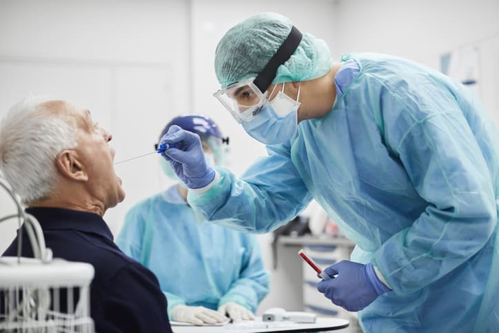 Doctor in PPE taking throat swab test from male patient