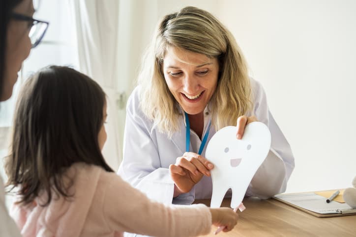 Dentist teaching little girl how to brush teeth during National Children's Dental Health Month