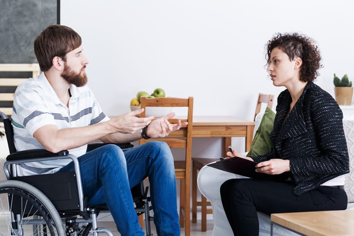 Young bearded man in wheelchair talking with occupational therapist