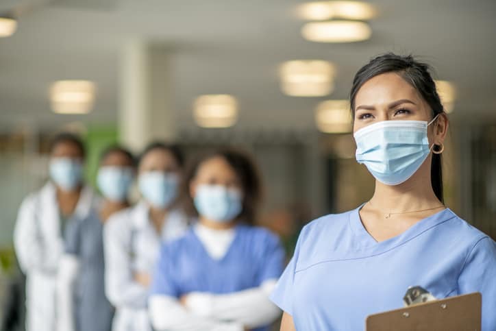 A diverse group of nurses stand in an institutional building in medical wear and face masks