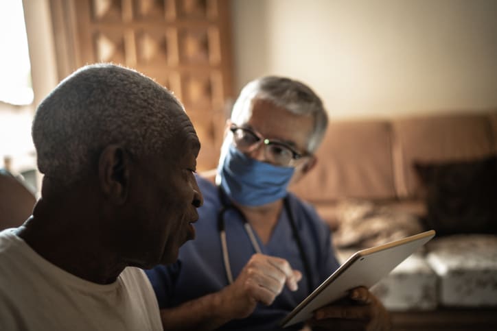 Health visitor and a senior African American man during home visit using digital tablet