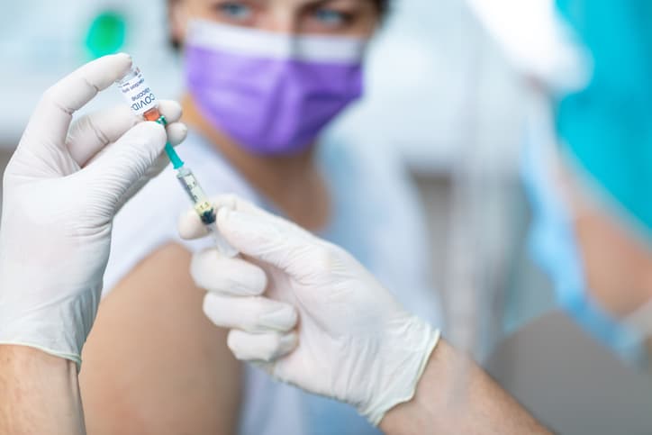 Doctor's hands in surgical gloves pulling COVID-19 vaccine liquid from vial to vaccinate female patient