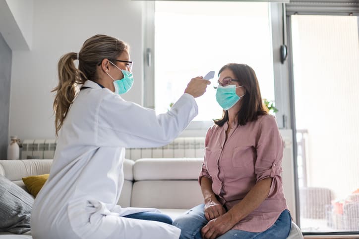 Healthcare worker at home wellness visit checks woman's temperature