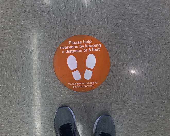 Sign telling people where to stand to honor 6-feet social distancing with a person's running shoes at bottom