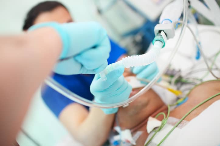 Medical doctor with assistant intubates male patient in the critical care unit.