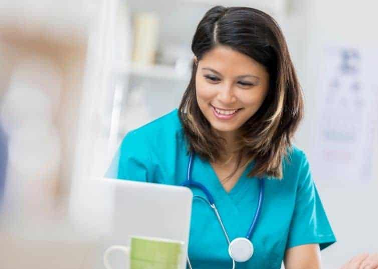 Female nurse in scrubs filling out nursing survey on laptop during break