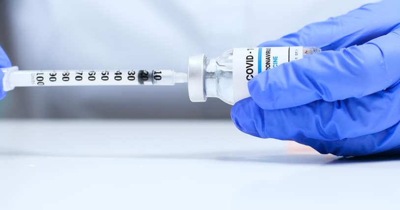 Close-up of female doctor hands in blue medical gloves with transparent liquid coronavirus Sars-Cov-2 vaccine bottle and syringe for injection
