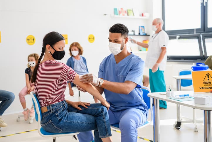 Young woman with face mask getting vaccinated, with others waiting for their vaccines in the background