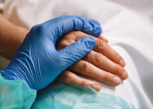 Close-up of nurse's gloved hand resting on patient's hand, practicing holistic heathcare