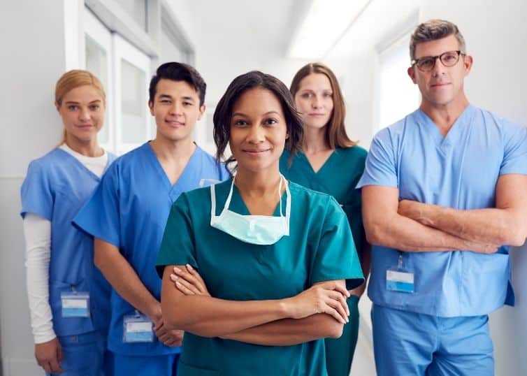 Group of diverse nurse heroes in scrubs stand proudly facing camera in hospital hallway