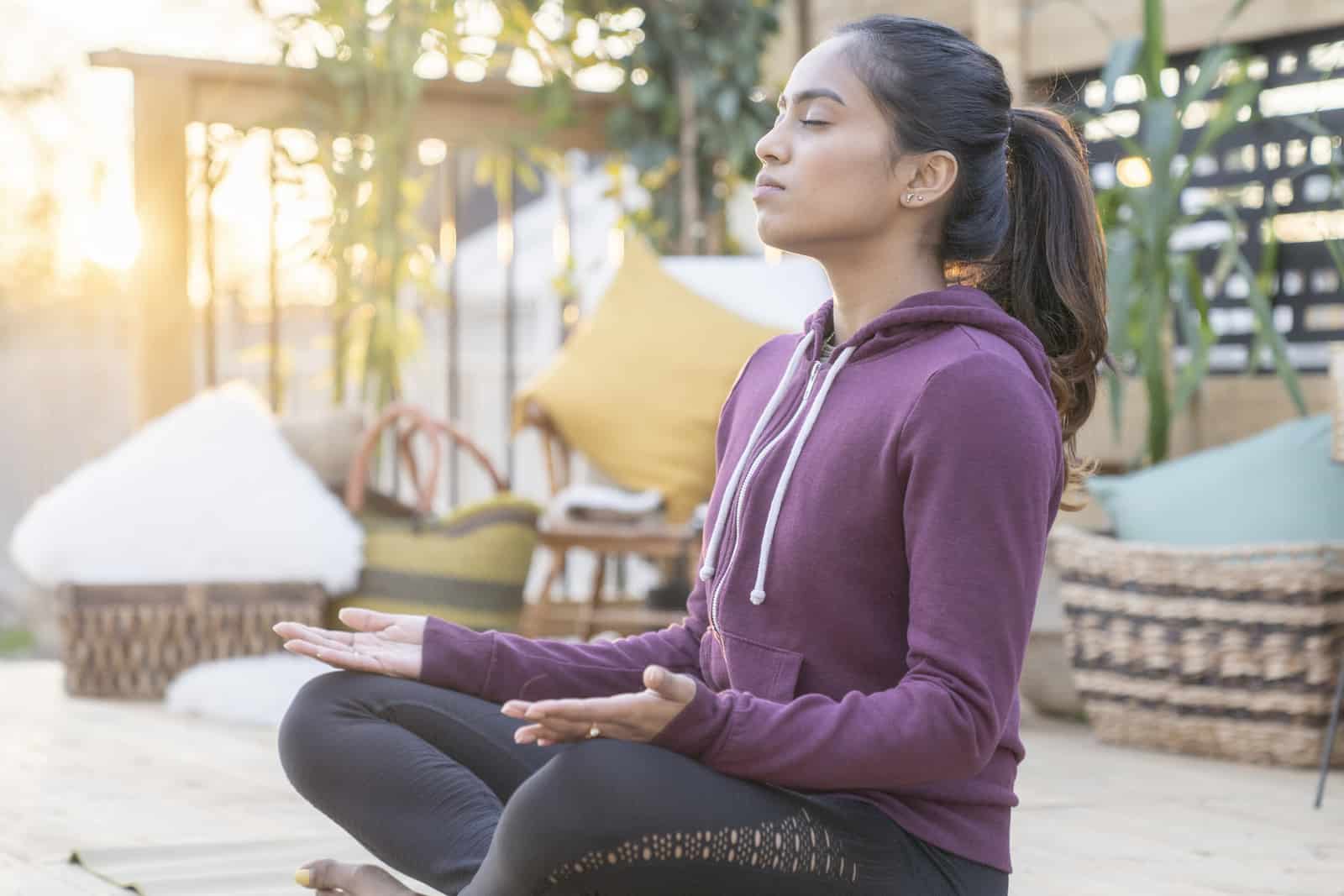 Beautiful mixed race female in her 20's doing relaxing yoga in her backyard while the sun sets behind her.