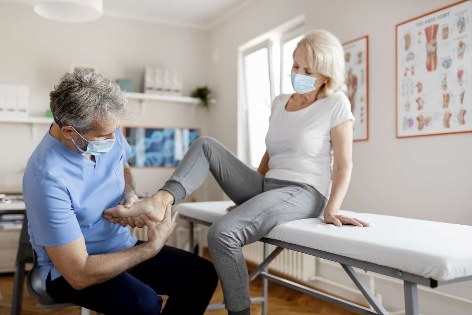 Massage therapist performs pain relief technique targeting fascia on mature female patient's foot