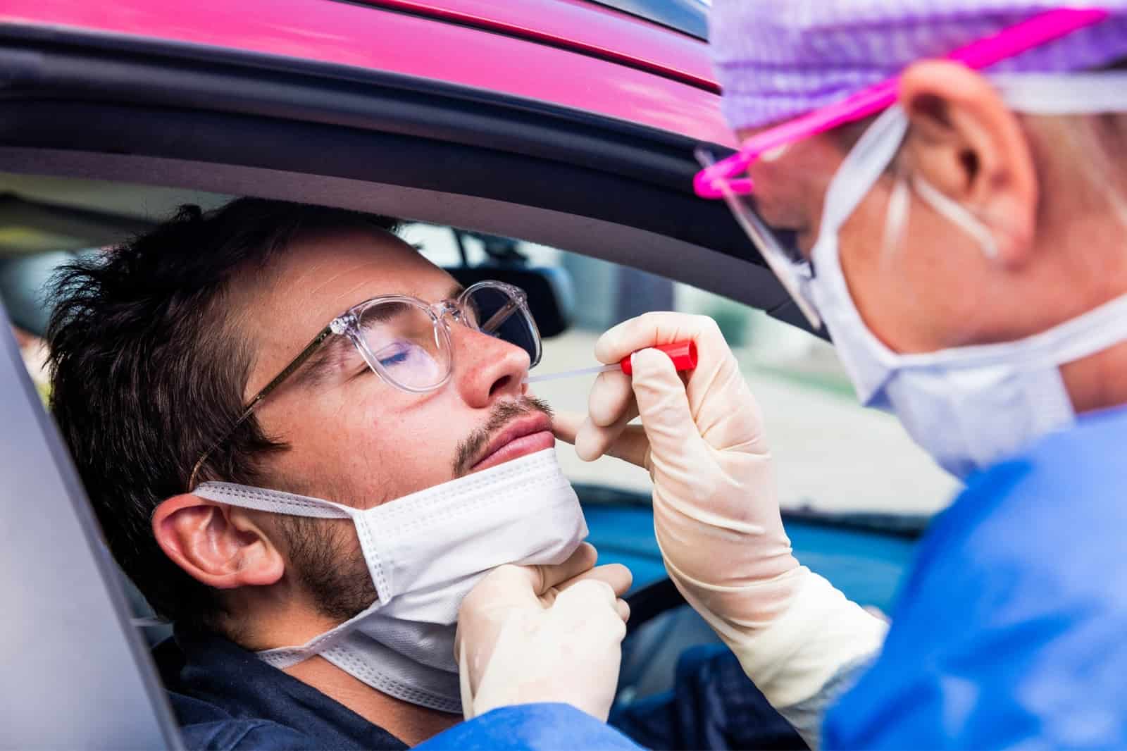 Health professional wearing PPE tests man for new COVID-19 variant at drive-up testing site