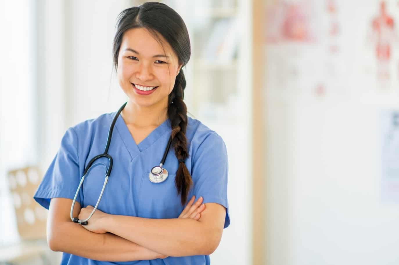 Successful happy young female nurse in scrubs smiling, posing with arms crossed