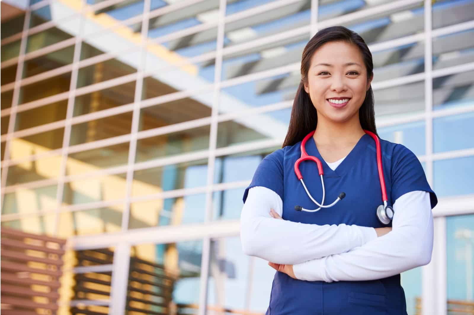Confident PhD-prepared nurse stands smiling outside of research hospital