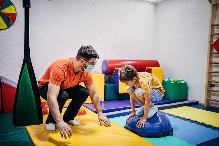 Male physical therapist and young boy exercising, pediatric physical therapy specialization concept