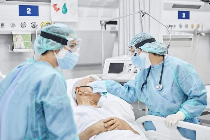 Proning COVID-19 patients. ICU nurses in full PPE prepare to turn elderly patient over in bed.