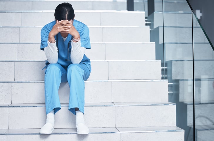 Tired nurse running on empty, sitting on hospital stairs with head in hands