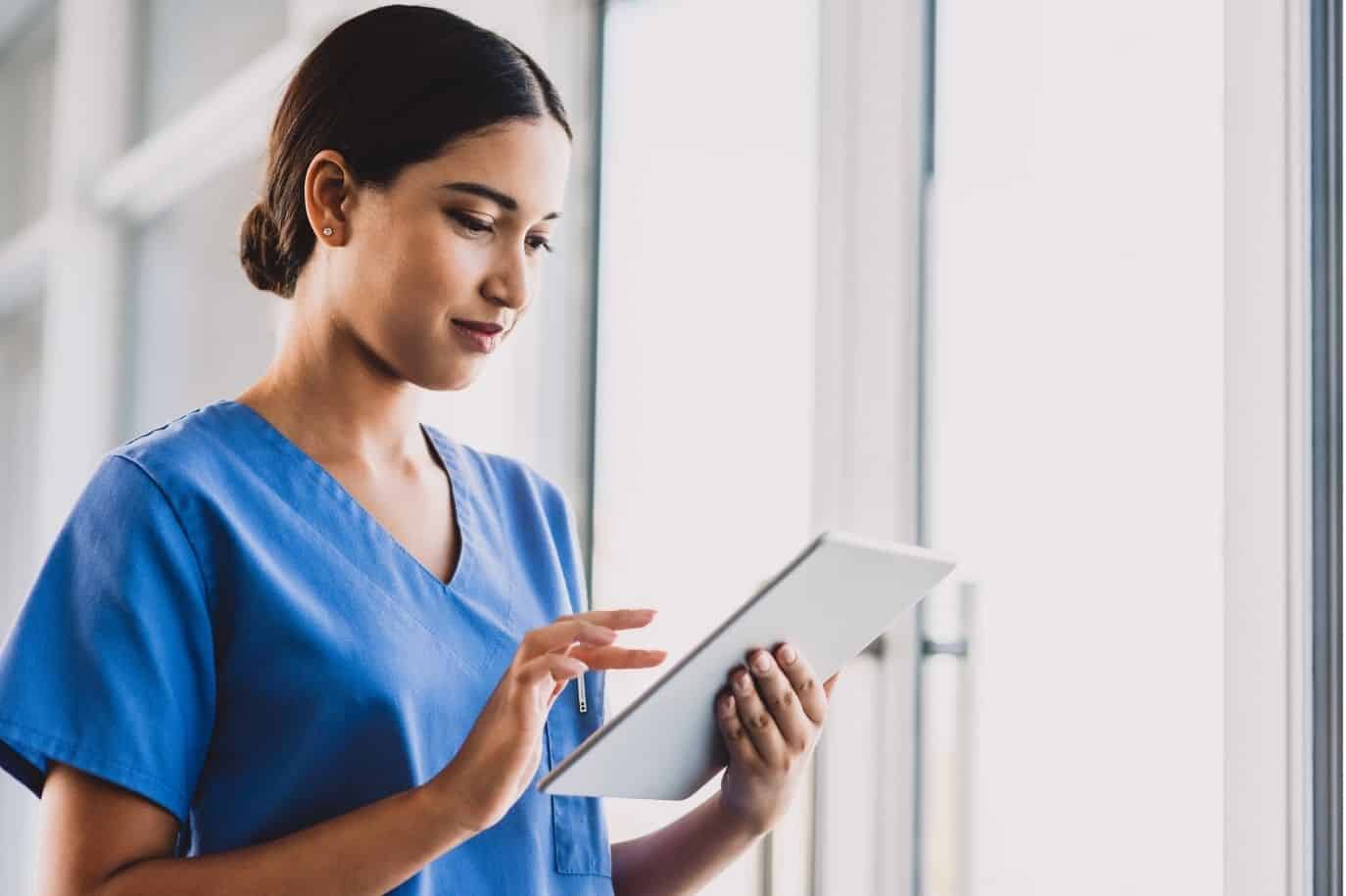 Healthcare professional in scrubs fills out salary survey on digital tablet