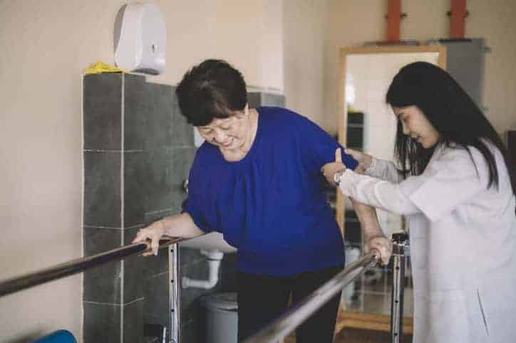 Caring asain female physical therapist helps senior woman stroke victim with body neglect in rehab center