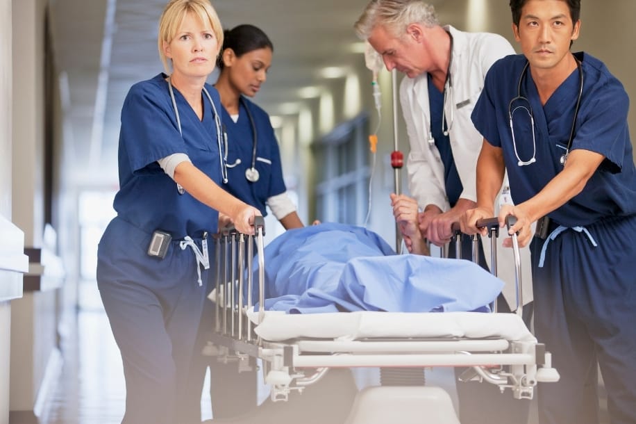 Emergency nurses and doctor quickly wheel patient bed down hospital hallway
