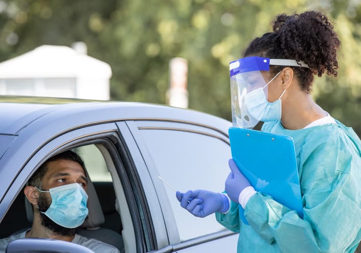 Drive through testing site for Covid-19 patients, healthcare worker in full PPE testing young man for R.1 variant