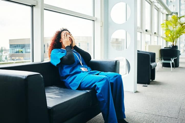 Stressed young female medical professional sitting on a sofa and taking break from work in hospital, sleep deprivation concept