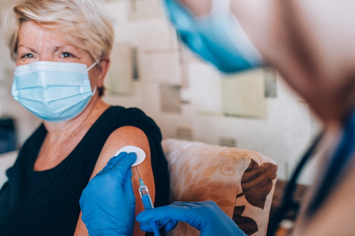 Senior woman getting a vaccine booster shot from her doctor in her home during the COVID-19 pandemic.