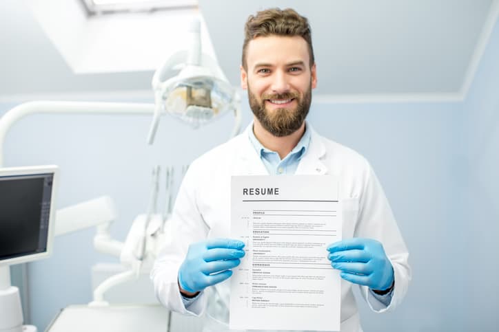 Professional male dentist holding dental resume for a new job standing at the dental office