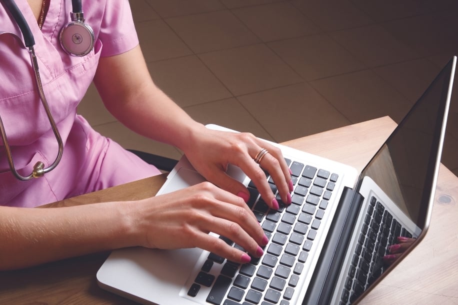 Close-up of a female nurse's hands typing on laptop