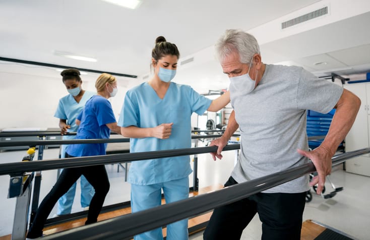 Group of physical therapists and patients in a rehab center wearing facemasks while doing their physical therapy, rehab during COVID-19 pandemic