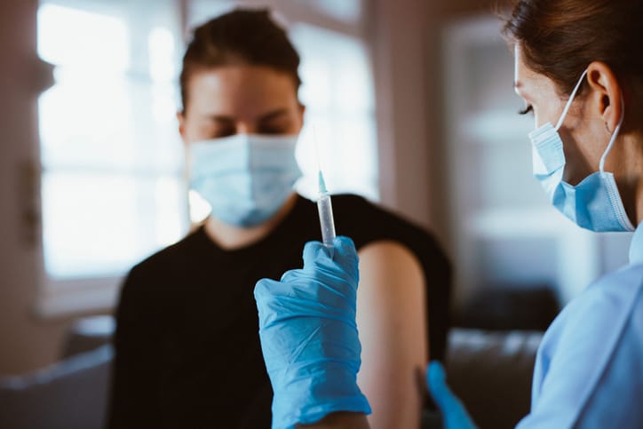 Nurse giving COVID-19 vaccine to young nursing student