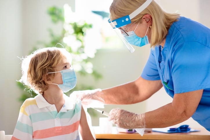Healthcare worker wearing mask, visor, and gloves injects Covid-19 vaccine in male child 5-11 years old.