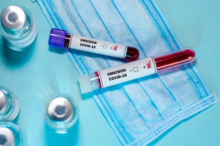 Test tube with positive Omicron COVID-19 test blood sample and vaccine bottle in the medical laboratory.
