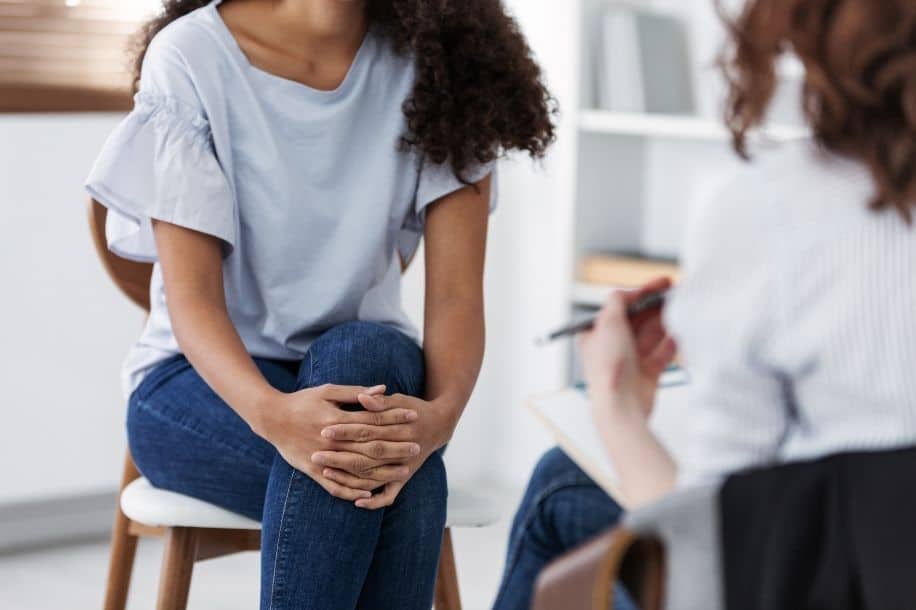Woman sits with legs crossed, meets with therapist or counselor. Period poverty concept.