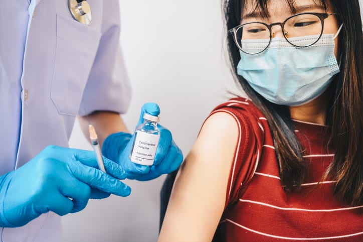 Close up of gloved hands holding a bottle of covid-19 vaccine and syringe before injection to adolescent female patient. Vaccine for kids 12-17 concept.
