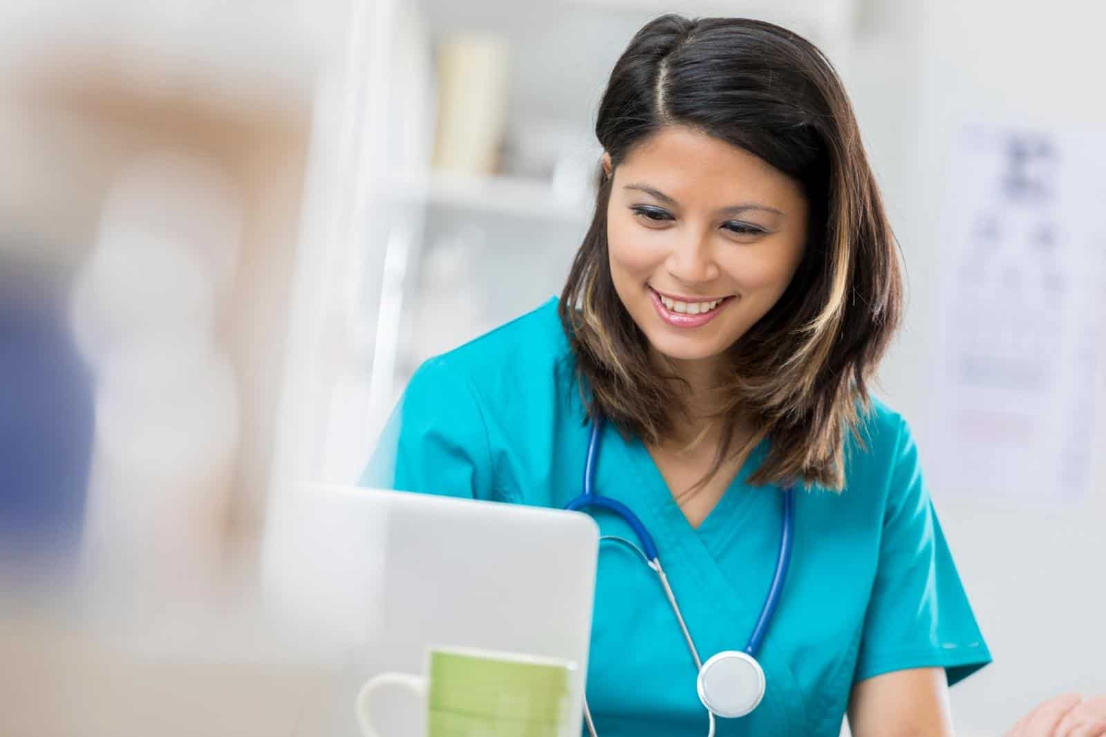 Smiling nurse reads up on the latest nursing news on laptop in office or hospital break room