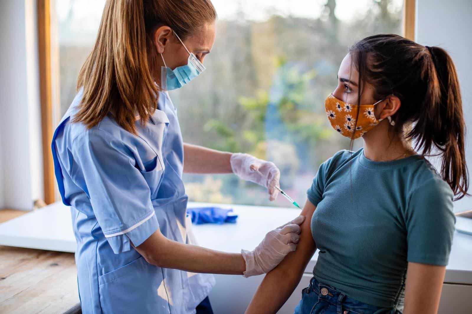 Teenage girl receives Pfizer vaccine booster dose from healthcare professional wearing mask and gloves