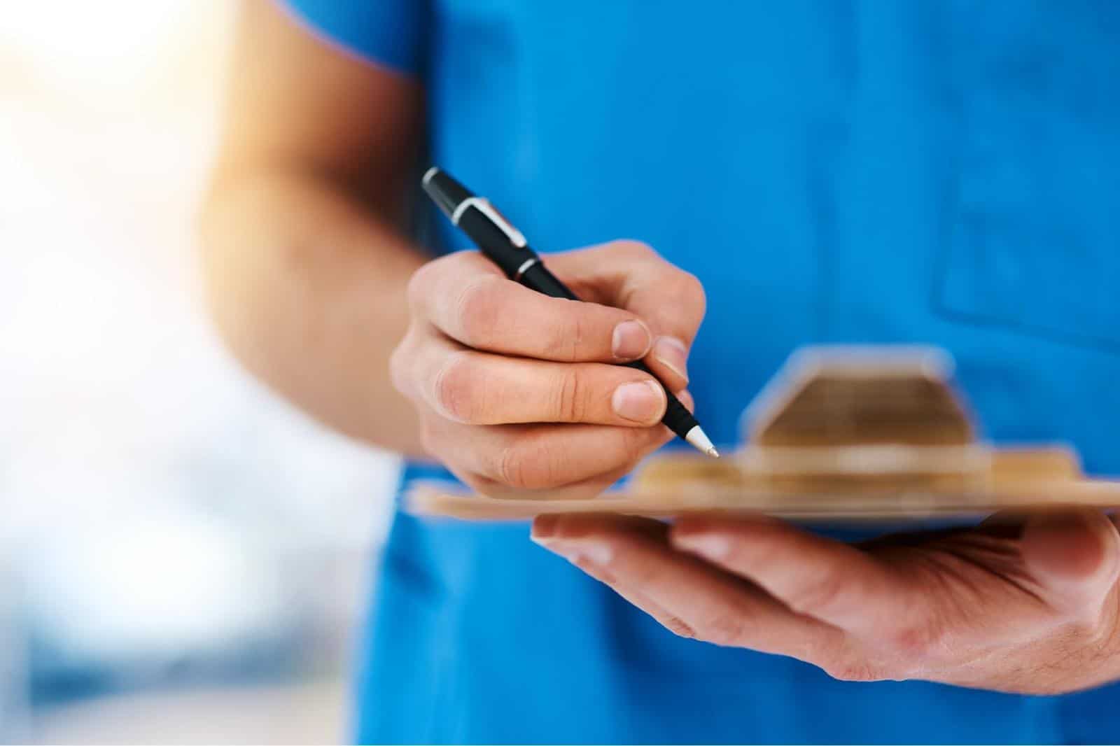 Closeup of nurse hands writing with pen on clipboard
