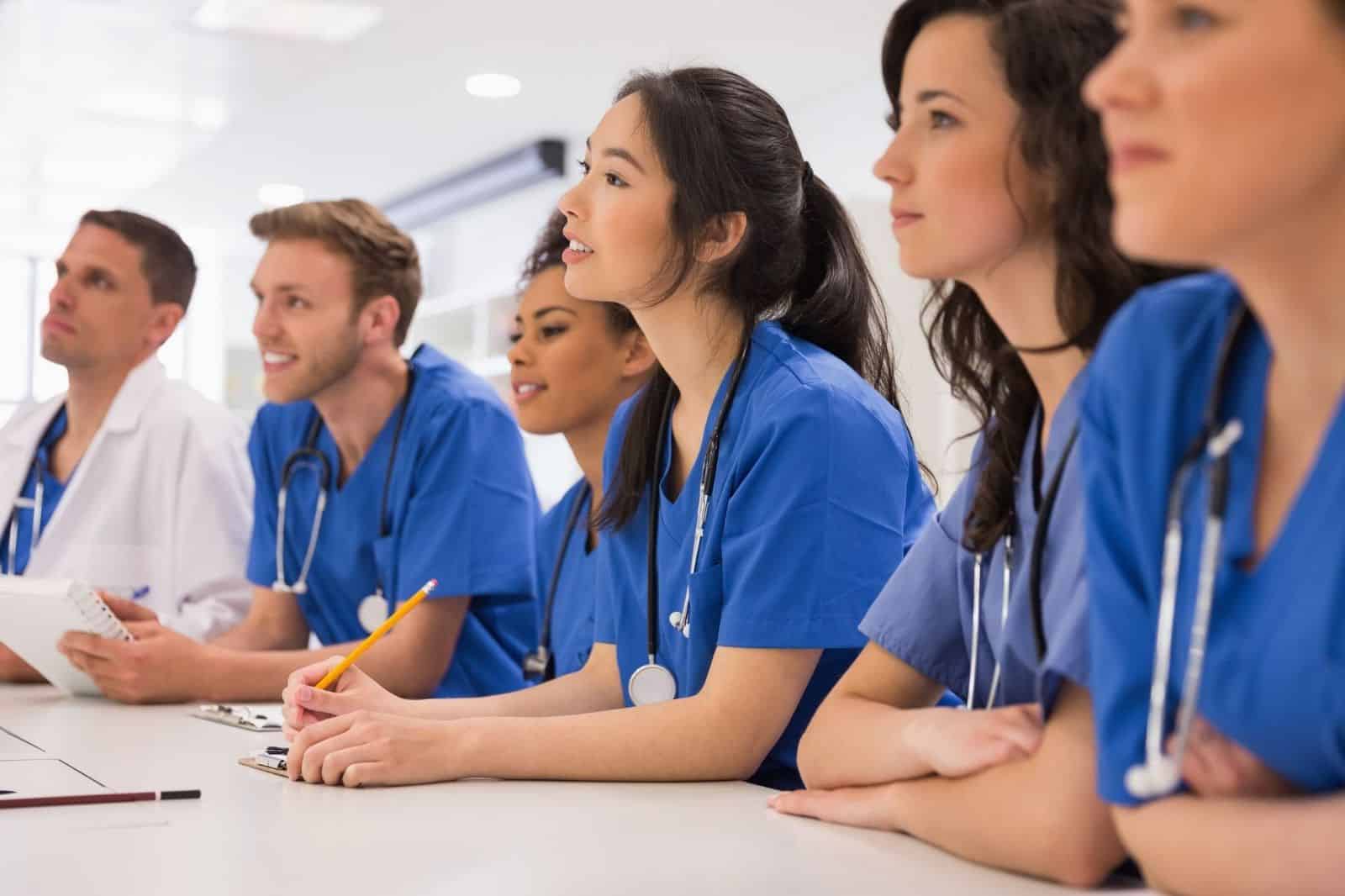 NP program students sit attentively in classroom, wearing medical scrubs