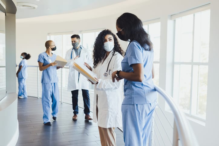 Black female chief nursing officer (CNO) talks with nursing staff member. Healthcare professionals wearing protective masks due to COVID-19.