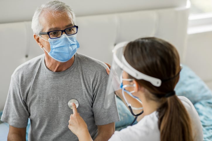 Health visitor using stethoscope to check senior man's heart health during home visit
