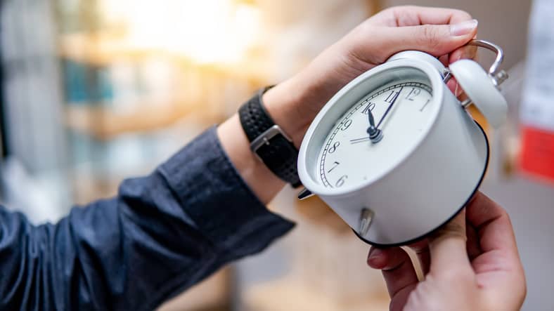 Male hand changing the time on white clock. Daylight Saving Time concept.